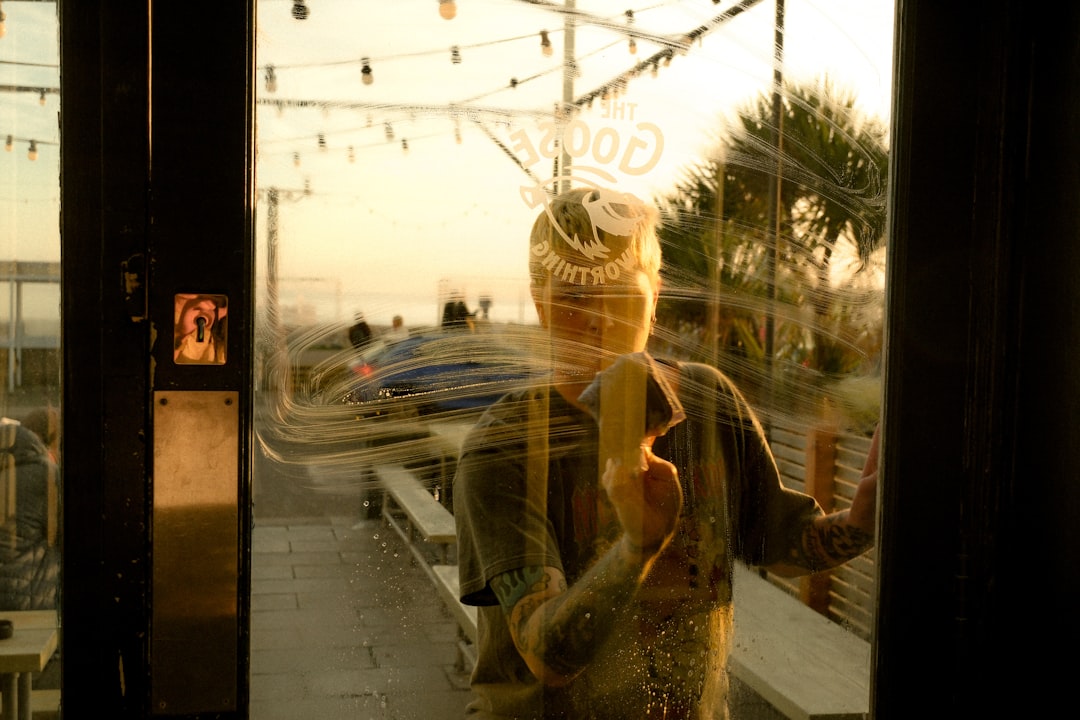 man-reflected-in-glass-door-looking-out-at-beach-osztsysuqmk